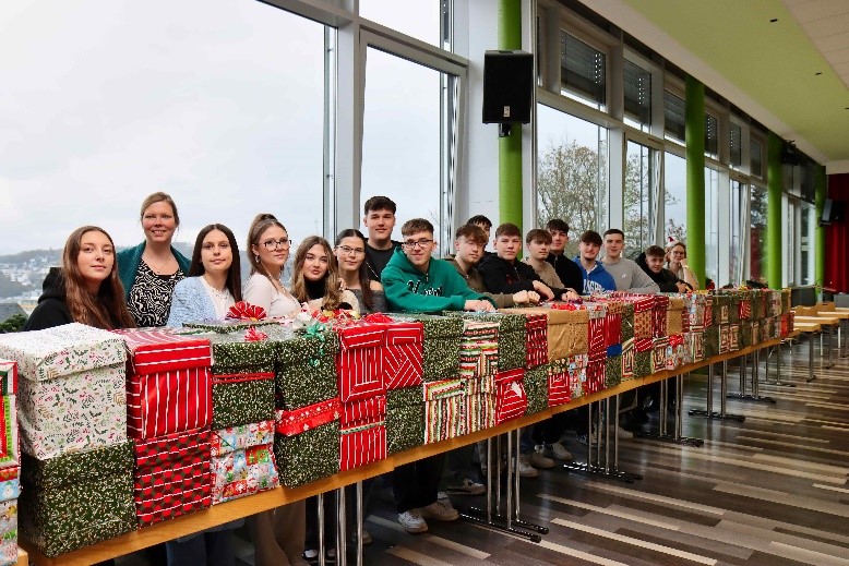 Es ist eine lange Reihe von 155 Weihnachtspäckchen mit glücklichen Schülerinnen und Schülern zu sehen.